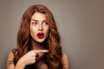 Fototapeta premium Surprised red head girl pointing finger. Excited redhead model woman pointing on background with empty copy space