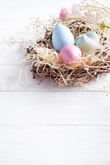 colorful easter eggs in small nest with on white wooden background, copy space. Holiday event