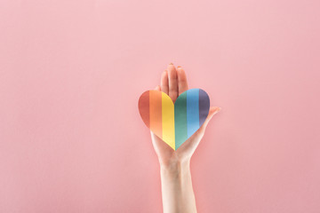 cropped view of woman holding rainbow colored paper heart on pink background, lgbt concept
