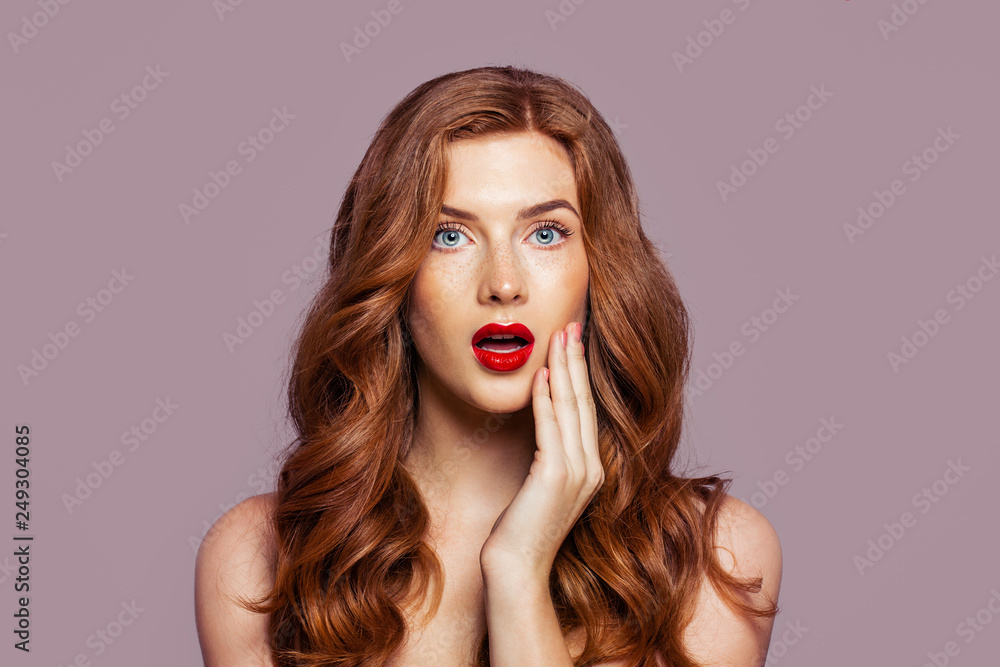 Wall mural Surprised woman with beautiful red hair on bright pink background. Redhead girl with opened mouth portrait