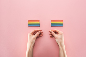partial view of female hands with paper rainbow flags on pink background, lgbt concept
