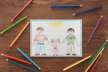 white paper with drawing of same sex family and multicolored pencils on wooden brown surface, lgbt...
