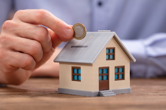 Person Inserting Coin In House Piggybank