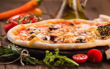 delicious Italian seafood pizza with ingredients on a dark wooden table (close).