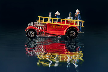 Toy red car with ladder and fire brigade on dark background with water and reflection.
