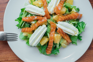 Salad with salmon, soft cheese and orange slices on a white plate