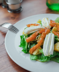 Salad with salmon, soft cheese and orange slices on a white plate