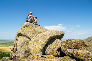 Guy gazing in the distance, while standing on top of a strange rock formation, during an Autumn hike with very hot weather, in Macin mountains, Romania
