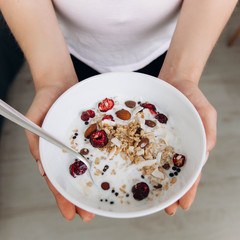A woman holds a bowl of muesli with berries in her hands