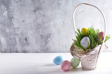 Easter basket filled with colorful hand painted Easter Eggs on grass over a light background