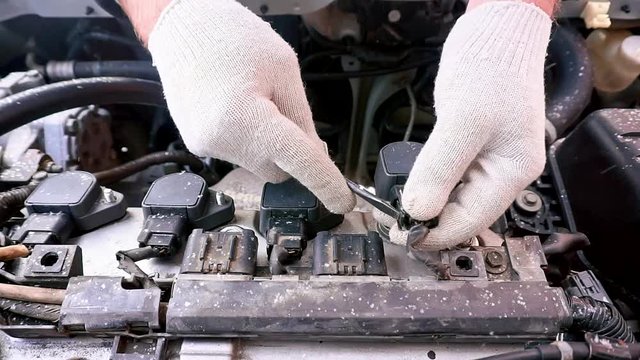 The car will not start, it's cold outside. A man removes the ignition coil and disconnects it from the car engine.
