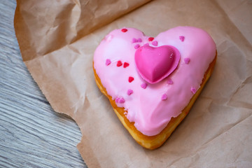 Naklejka na ściany i meble Pink heart donut over the brown paper bag on the wooden table. The closeup food photo.