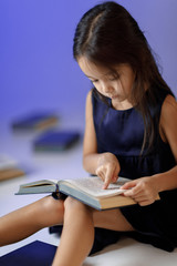 portrait of cute little girl in dark blue dress is reading a book. child and a lot of books. Children and education.