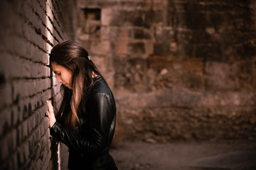 Angry and pensive adult young woman leaning head against a brick wall, reflecting on her sadness and inner personal crisis.
