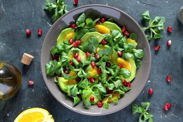 Green salad with avocado, orange and pomegranate in a bowl over dark background. Top view. Vegetarian and vegan food. Diet food.
