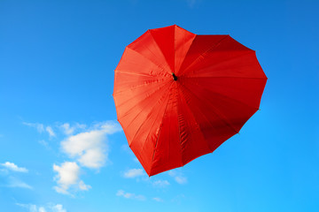 Red, scarlet umbrella in the shape of heart against blue sky on clear, sunny day. Valentine's day concept.