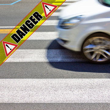Black and white pedestrian crossing with white car on background - concept image with danger text written on it