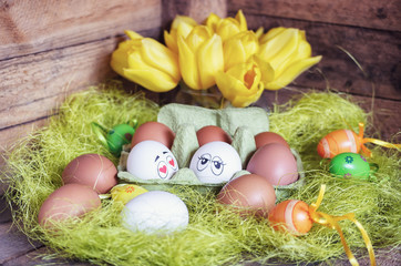 Easter composition with white and brown eggs in box with two eggs plastered with funny faces