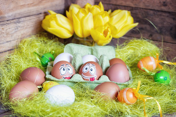 Fototapeta na wymiar Easter composition with white and brown eggs in box with two eggs plastered with funny faces