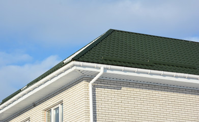 Brick house with green metal roof and rain gutter pipeline