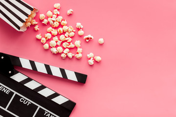 Film watching concept. Clapperboard and popcorn on pink background top view copy space