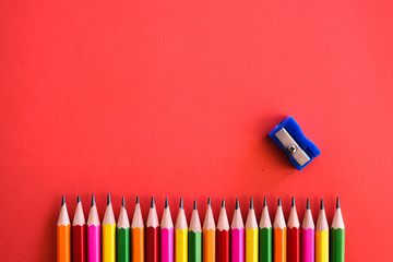 Colorful pensils align in a row shot  with a sharpener on a plain isolated red background as wallpaper.