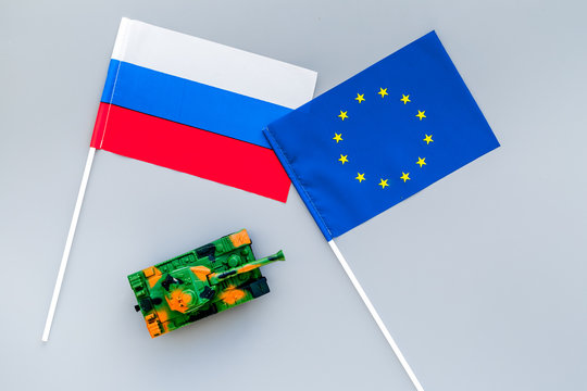 War, confrontation concept. European Union, Russia. Tanks toy near european and russian flag on grey background top view