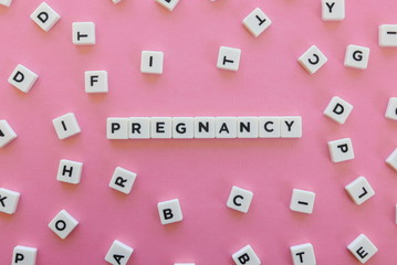 Pregnancy word made of square letter word on pink background.