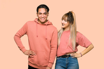 Young couple posing with arms at hip and smiling over pink background