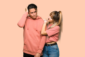 Fototapeta premium Young couple having doubts while scratching head over pink background
