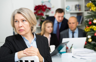 Upset mature woman at office on background with coworkers