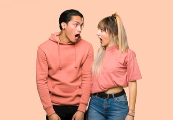 Young couple with surprise and shocked facial expression over pink background