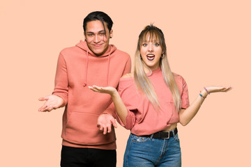 Young couple making unimportant gesture while lifting the shoulders over pink background