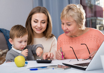 Fototapeta premium Aged woman is mastering technology near laptop with her daughter and grandson