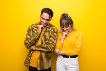 Young couple over vibrant yellow background looking down with the hand on the chin © luismolinero