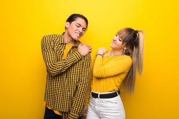 Young couple over vibrant yellow background suffering from pain in shoulder for having made an effort