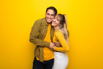 Young couple hugging on vibrant yellow background.