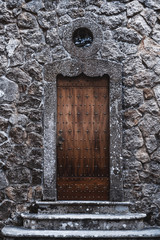 Fototapeta premium A vertical shot of a beautiful antique wooden riveted door in a stone wall with a small round window above and old stony steps in the bottom, Sintra, Portugal