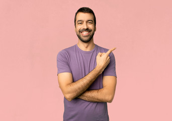 Handsome man pointing to the side to present a product on isolated pink background