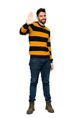 Fototapeta premium Full-length shot of Handsome man with striped sweater saluting with hand with happy expression on isolated white background