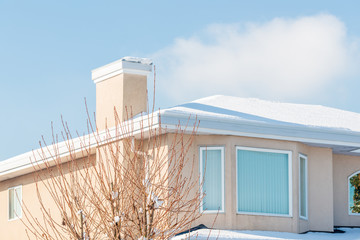 A typical american house in winter. Fragment of a house with roof and window covered by snow. Daylight and blue sky.