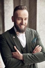 Smiling bearded man in brown green three-piece suit, bow tie posing near columns in Venice, Italy