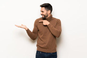 Handsome man over white wall holding copyspace imaginary on the palm to insert an ad