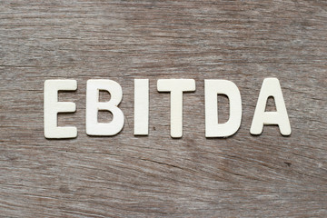 Alphabet letter in word EBITDA (abbreviation of earnings before interest, taxes, depreciation and amortization) on wood background