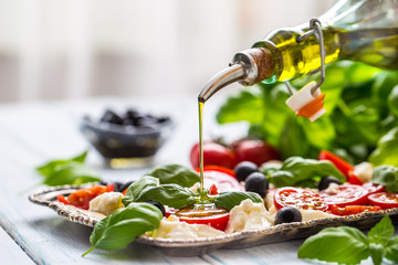 Pouring olive oil on caprese salad. Healthy italian or mediterranean meal