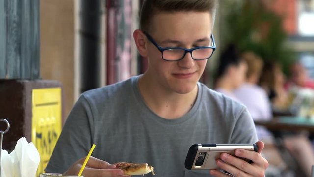 Young, teenage boy watching movie on smartphone, eat pizza in cafe
