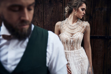 Wedding couple posing near wooden gate in Venice. Woman in elegant luxury ivory dress and messy updo hair, man in green suit with bow tie