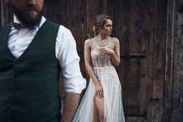 Fototapeta premium Wedding couple posing near wooden gate in Venice. Woman in elegant luxury ivory dress and messy updo hair, man in green suit with bow tie