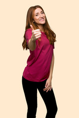 Young redhead girl giving a thumbs up gesture because something good has happened on isolated yellow background