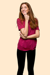 Young redhead girl looking to the side with the hand on the chin on isolated yellow background